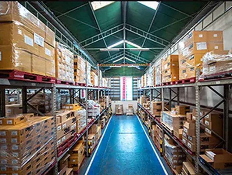 Photograph of a pallet-racked warehouse aisle stacked to the roof, picked by hand from the racks &mdash; no conveyors, sorters or robotics